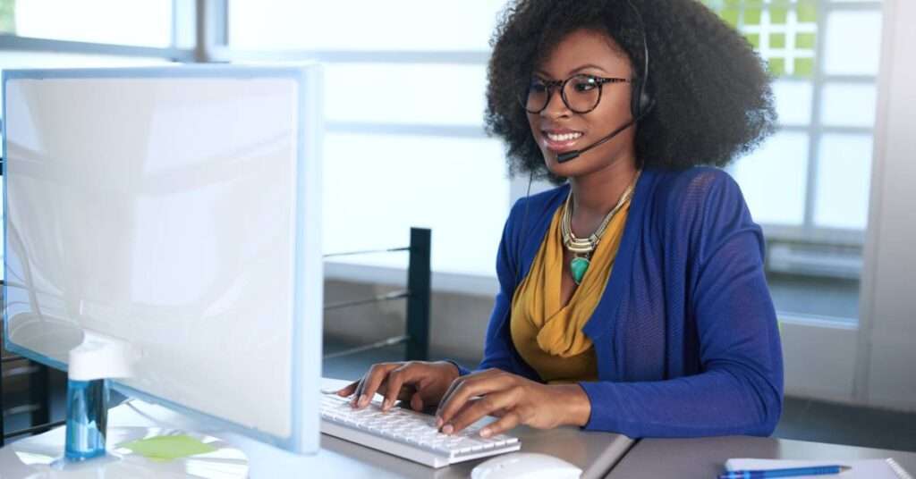 A portrait of a smiling customer service representative working at her computer desk while wearing a headset.