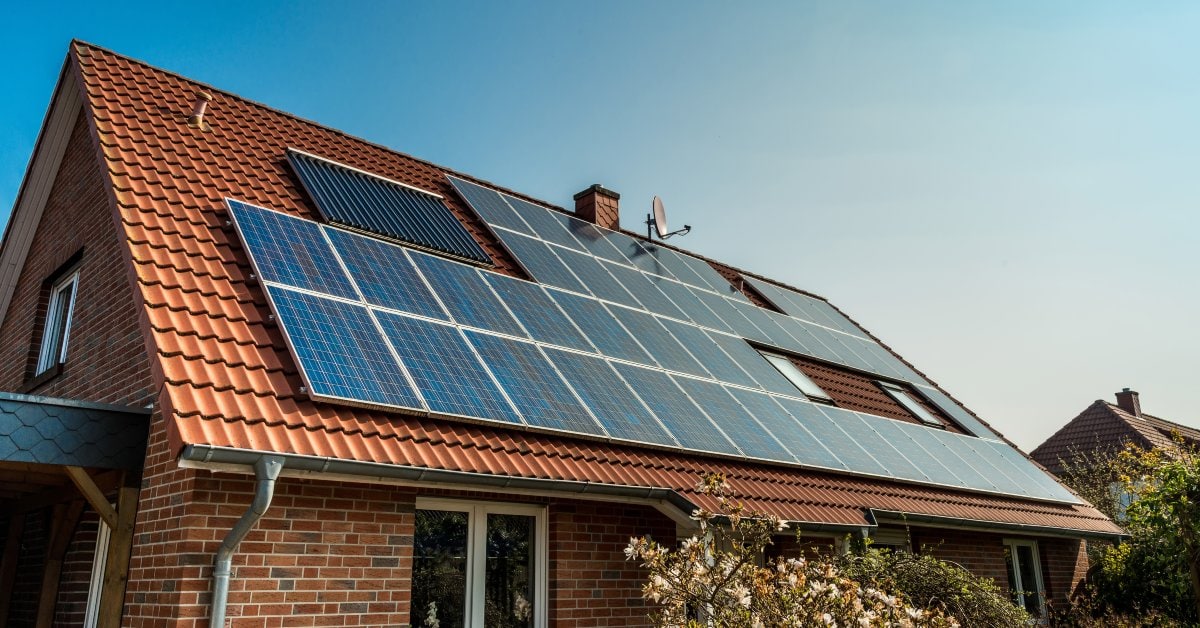 Multiple sets of blue solar panels on a classic red brick home with matching terracotta tiles, all under a bright blue sky.