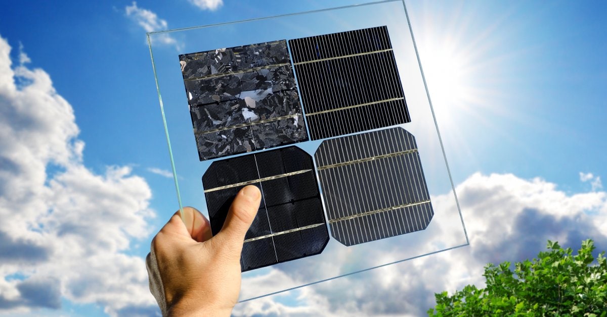 A hand holding up a clear glass panel, with different samples of solar cells, up to the bright, shining sun.