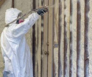 A person wearing protective gear sprays Greenlink foam insulation onto interior wall studs in a building under construction or renovation. A person wearing protective gear sprays Greenlink foam insulation onto interior wall studs in a building under construction or renovation.